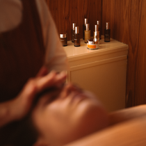 Person receiving a facial massage with skincare products on a wooden shelf in the background