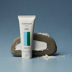 DAMDAM Skin Mud Pure Mask tube beside a stone and kaolin clay powder
