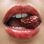 Glossy red-tinted lips wearing Herbar The Lip Butter Jujube, biting into a dried jujube fruit