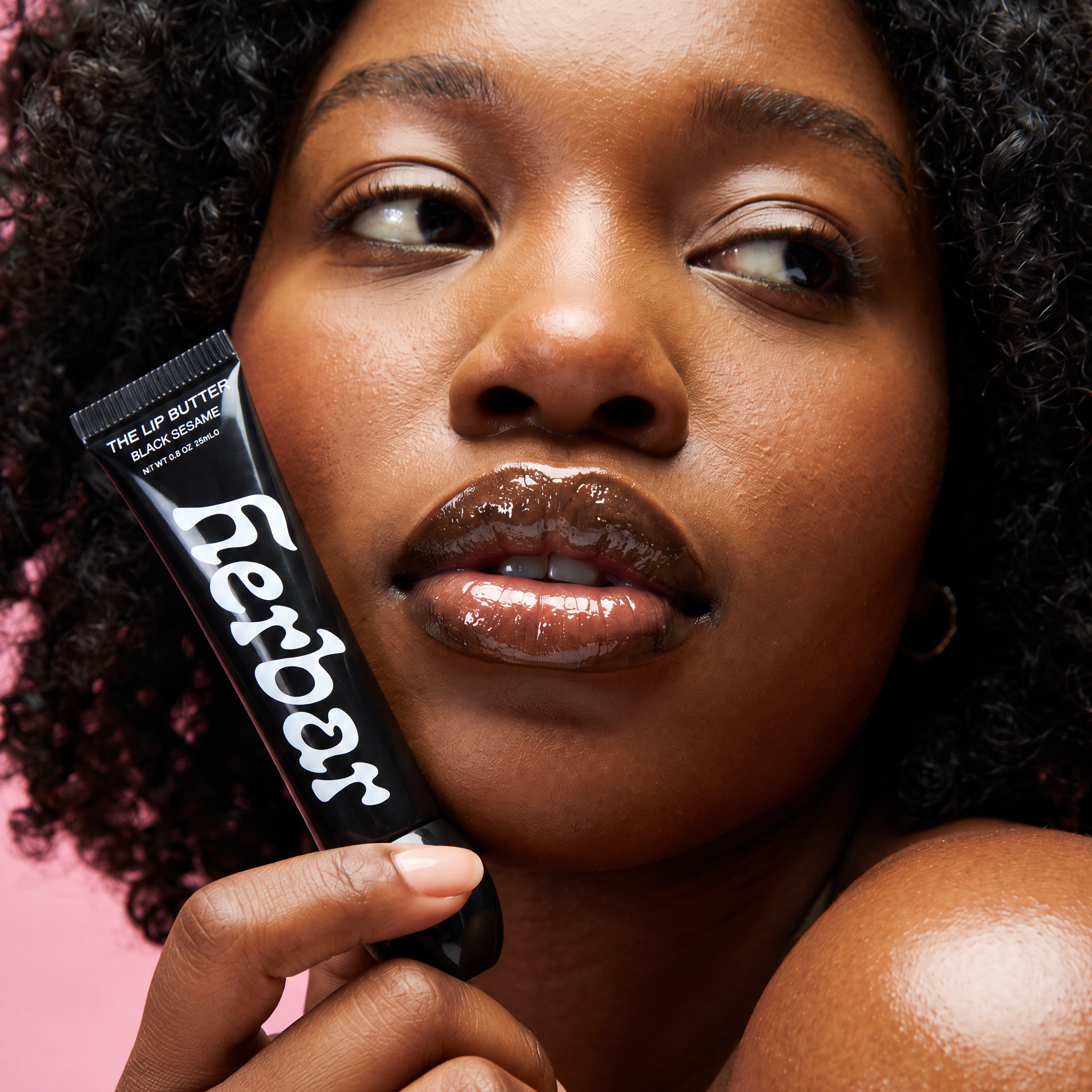 Model holding Herbar The Lip Butter Black Sesame next to her glossy, hydrated lips