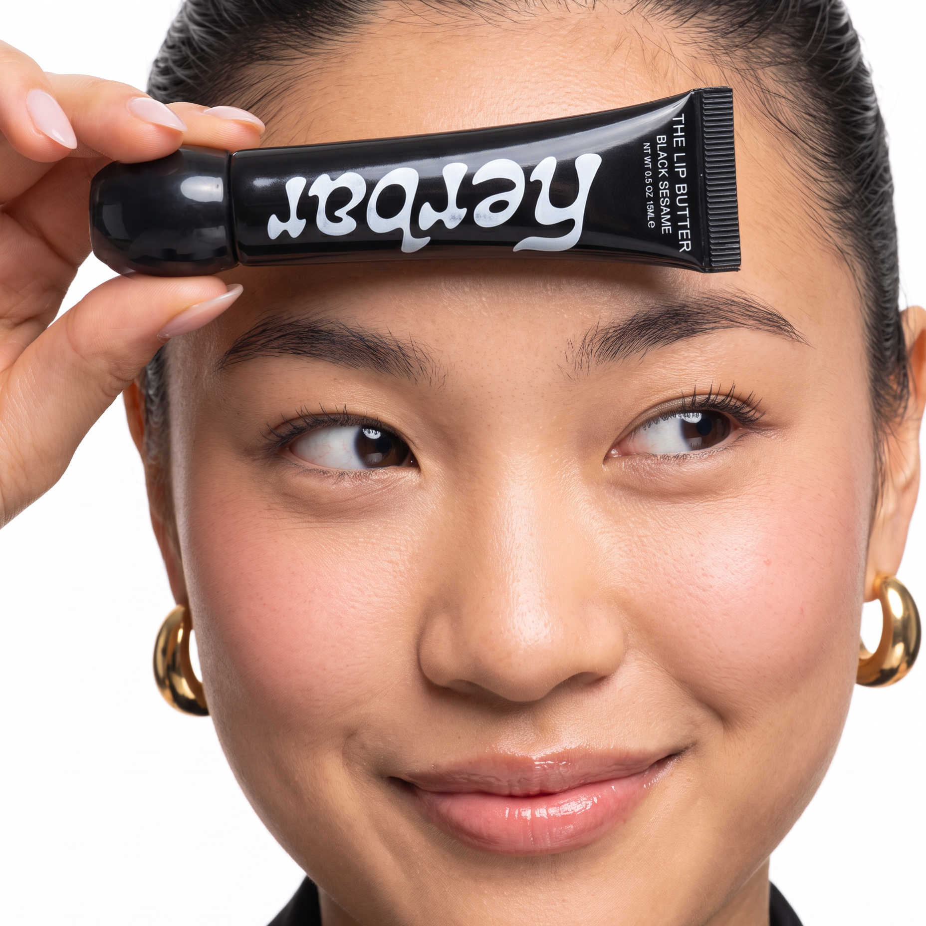 Smiling model holding Herbar The Lip Butter Black Sesame tube to her forehead