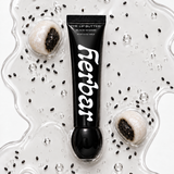 Herbar The Lip Butter Black Sesame tube on a clear buttery texture swatch scattered with sesame seeds