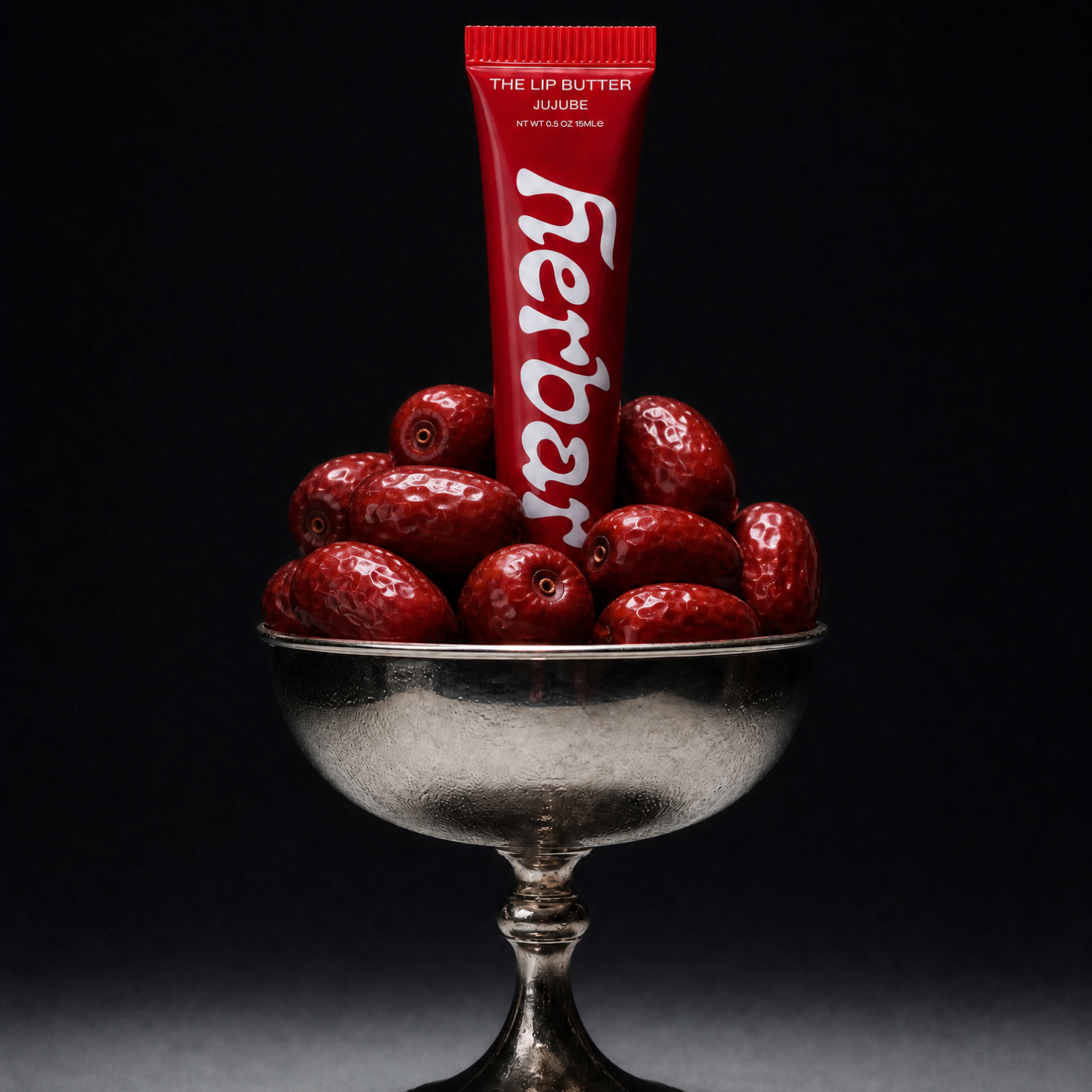 Herbar The Lip Butter Jujube tube resting in a silver bowl of red jujube fruit