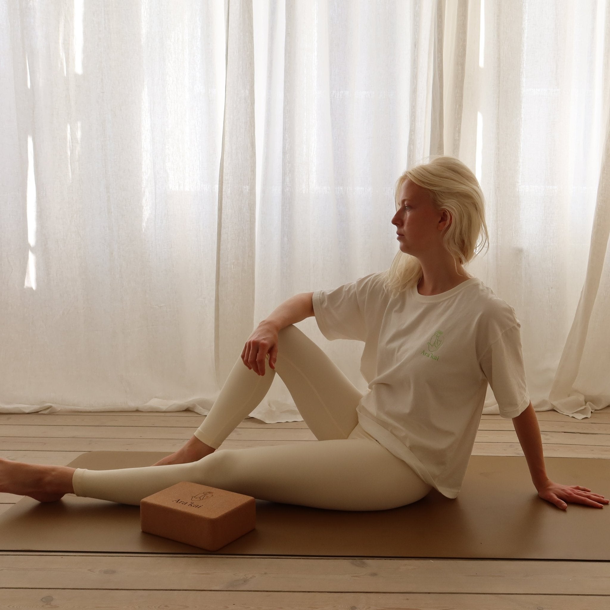 Woman in white yoga attire seated on mat in serene room with soft curtains