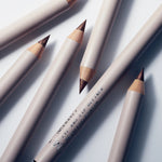 Several Manasi 7 Eye and Lip Definer organic wooden pencils scattered on a white surface