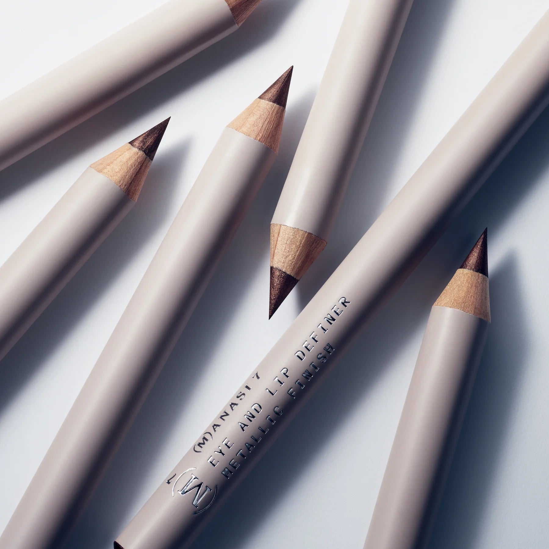 Several Manasi 7 Eye and Lip Definer organic wooden pencils scattered on a white surface