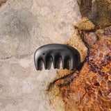 Sándor Scalp Gua Sha in black Bian stone resting on natural rock by water